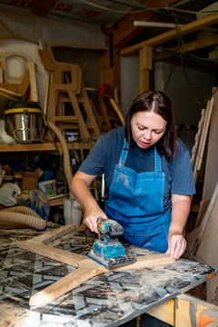 Woman in blue apron sanding or shaping wood in a workshop
