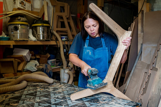 Woman in blue apron sanding or shaping wood in a workshop