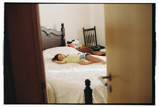 Child sleeping on white bed with open door view