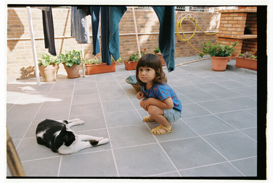 Child squatting beside cat on tiled patio