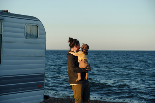 Father Holds Child While Standing by the Ocean at Sunset