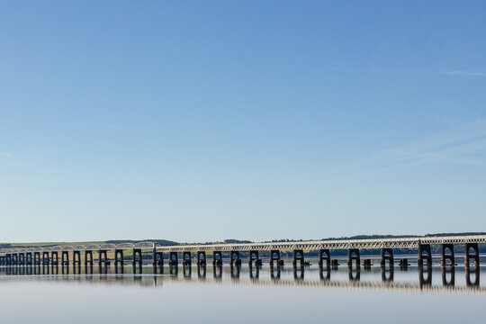 Long Wooden Bridge Spans Calm Water Under Clear Blue Sky
