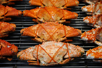 Steamed red crabs tied with rubber bands served on a black plate over a grill. Delicious fresh seafood delicacy ready for a meal, featuring vibrant orange shells and texture.