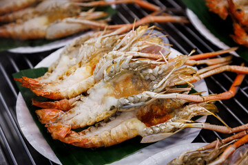 Grilled giant river prawns with creamy orange roe served on a white plate with banana leaf. Traditional Thai seafood delicacy, freshly cooked on a charcoal grill.