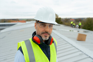 Confident man construction worker wearing safety gear on roof
