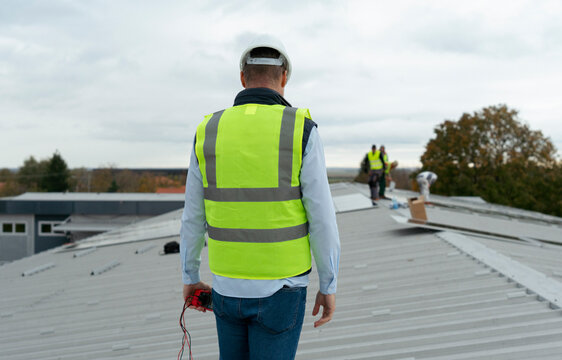 Construction worker supervising roofing contractors on building roof
