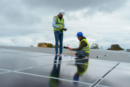 Engineers inspecting solar panels on a rooftop under cloudy sky
