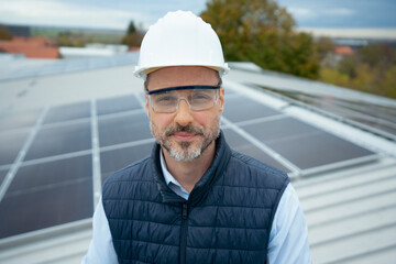 Technician wearing hard hat and safety glasses on rooftop solar panels