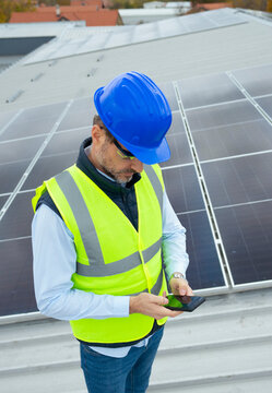 Engineer inspecting solar panels on rooftop with tablet
