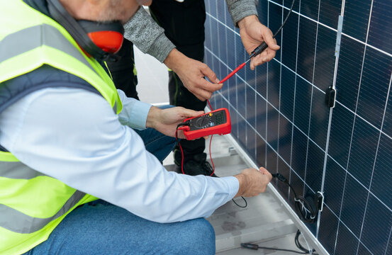 Technicians checking solar panel voltage with multimeter
