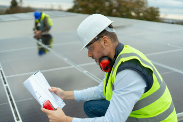 Engineer inspecting solar panel installation plans on a rooftop
