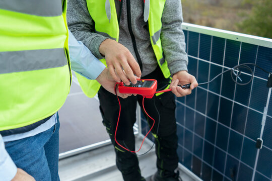 Technicians checking solar panel performance with multimeter
