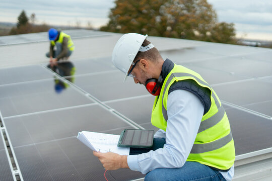 Engineers installing solar panels checking plan on rooftop
