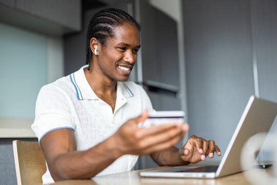 Smiling American Man Using Laptop and Credit Card in Modern Kitchen 