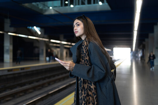 Woman waiting on subway platform holding phone