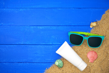 Cream tube with sunglasses and sand on blue wooden. Sea summer vacation background with space for the text. Top view
