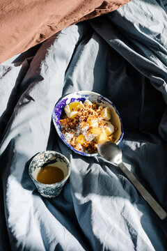 Yogurt bowl set on unmade sheets alongside a coffee lit by sunlight