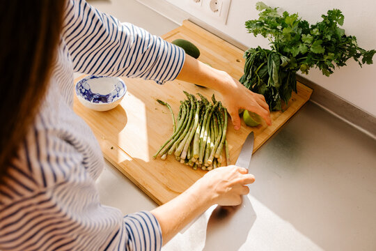 Woman choping asparagus and lemons while preparing food at home
