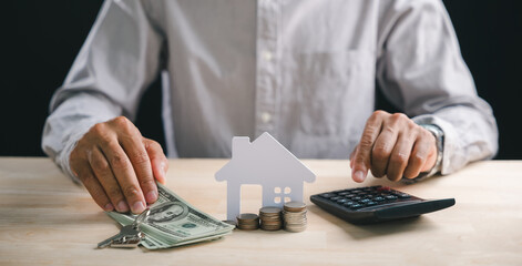 Hands calculating home interest rates for property loan, money, house model on desk with keys, coins, conceptualizing real estate investment mortgage planning