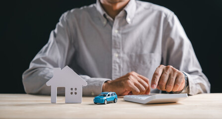 Business person calculates home property loan, real estate, or insurance concept, hands operate calculator near miniature house and new car models for future financial planning