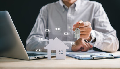 Real estate agent hand holds house key, desk features paper home model and property document, laptop screen shows mortgage loan for buying home, investors plan future ownership