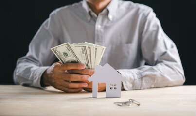 Property purchase concept shows hands holding dollars, keys beside paper house model representing real estate investment, home ownership finance planning for new estate loan
