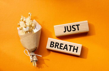 Just Breathe symbol. Wooden blocks with words Just Breathe. Beautiful orange background with bouquet of flowers. Business and Just Breathe concept. Copy space.