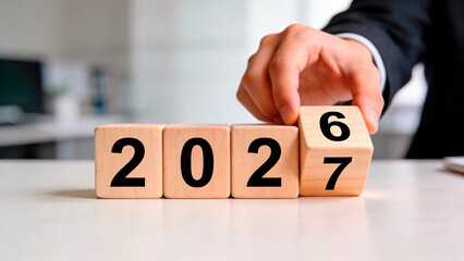 Hand adjusting wooden number blocks showing 2026 and 2027 values. Business concept of future planning and strategy. 