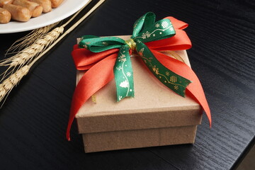 Christmas gift boxes with red and green ribbon, wreath garland, candy cane, santa sock, bauble and golden bells on black wooden table. Blank background mockup with copy space for adding text