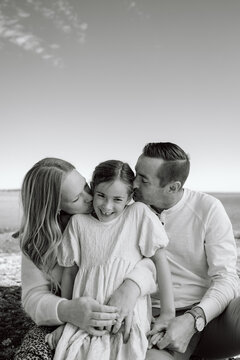 Candid family moment on the beach: parents kiss daughter, warm e