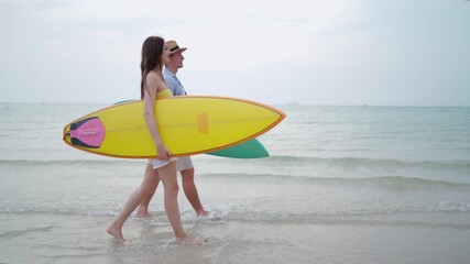 Young couple walking along the beach with surfboards.