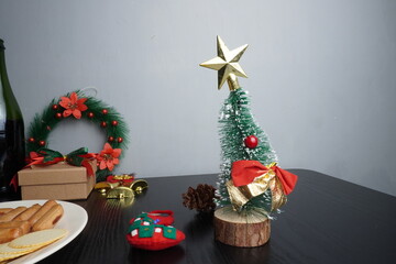 Christmas gift boxes with red and green ribbon, wreath garland, candy cane, santa sock, bauble on black wooden table with festive holiday decoration and some traditional food. Blank background mockup 