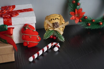 Christmas gift boxes with red and green ribbon, wreath garland, candy cane, santa sock, bauble on black wooden table with festive holiday decoration and some traditional food. Blank background mockup 