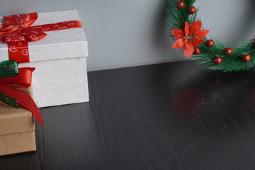 Christmas gift boxes with red and green ribbon on black wooden table with festive holiday decoration and some traditional food. Blank background mockup with copy space for adding text, logo, product, 