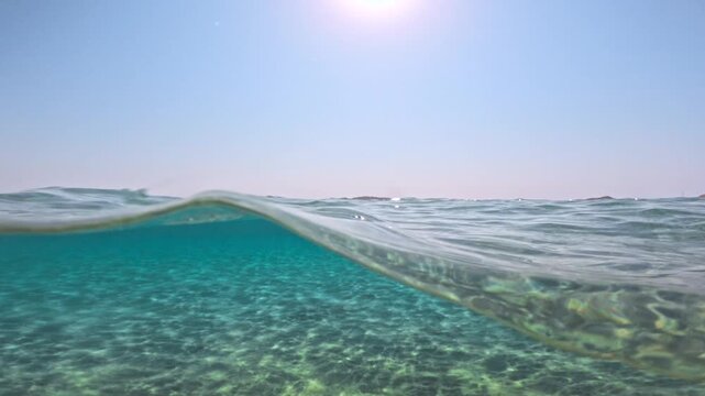 Slow motion half underwater waves in crystal clear turquoise sea under sun in blue sky