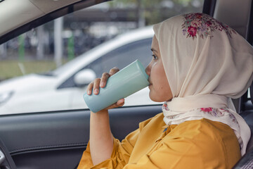 A young Indonesian Muslim woman drinking water before driving