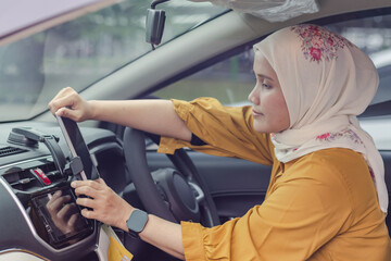 A young Indonesian Muslim woman placing her mobile phone in a holder on the dashboard of her car