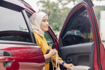 A young Indonesian Muslim woman has arrived at her destination and getting out of her car