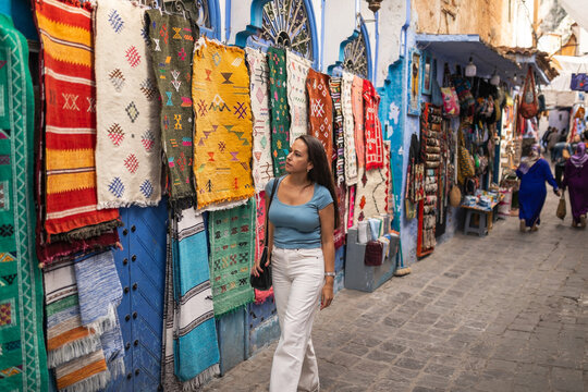 Woman walking past hanging rugs on a blue street in Chefchaouen