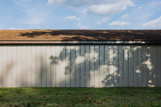 Tree shadows on metal building wall with shingle roof