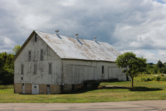 Weathered white barn with tree under cloudy sky