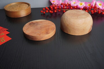 Empty background of a dark wooden tabletop with cherry blossom decorations, a bamboo dimsum steamer, and an empty plate for Chinese Lunar New Year celebration.
