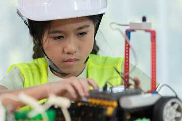 Focused young girl wearing hard hat and safety vest building a robotic vehicle, symbolizing STEM education, innovation and hands on learning in engineering and technology for kids.