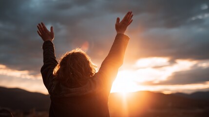 Worship and prayer at sunset beneath a glowing sky and mountains, uplifting silhouette with raised arms showing joy, faith and divine connection, contemplative person reaching toward the light