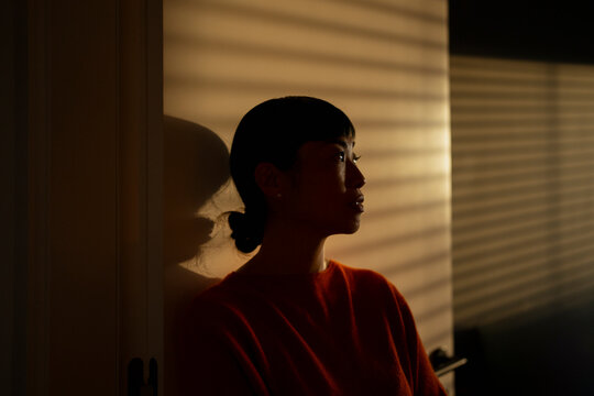 Woman contemplating during golden hour with blinds shadow
