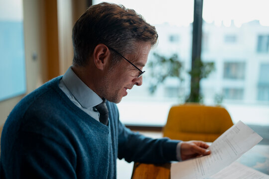 Businessman reading document, analyzing business paperwork in office
