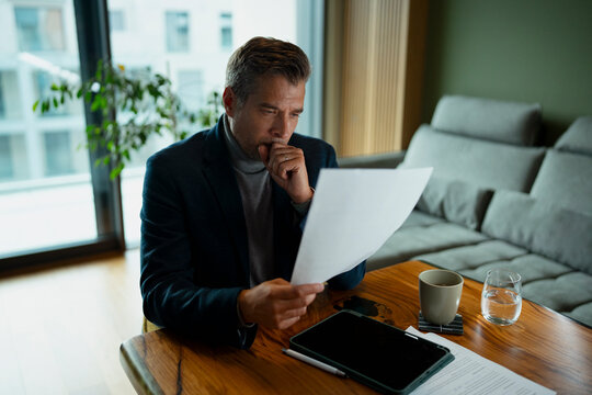 Concerned businessman reading financial document at home office
