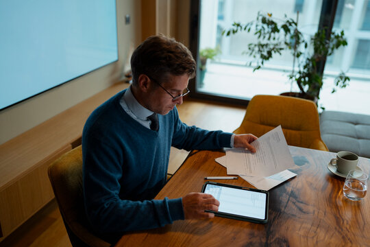 Man managing finances at home office using tablet and documents
