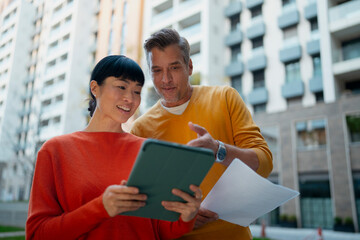 Diverse couple discussing real estate projects on tablet outdoors
