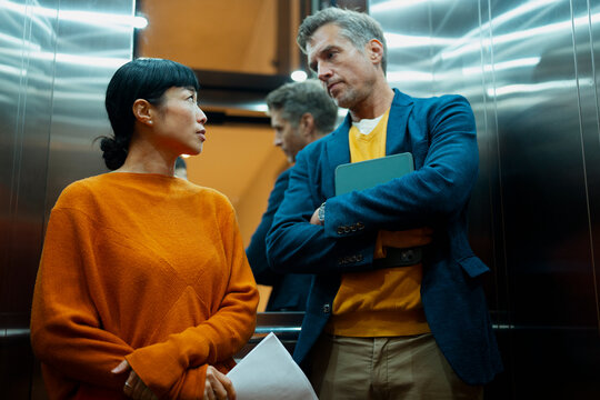 Business colleagues having serious conversation in modern elevator